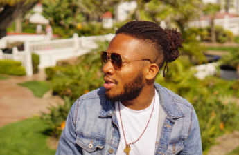 Man with locs and sunglasses looking to the right on a sunny day
