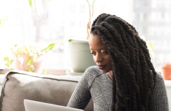 Black woman with marley braid extensions researching on her laptop. Meant to represent woman researching questions to ask a loctician