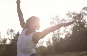 black man in white tanktop in a stretching pose exercising with locs