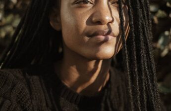 black woman with long locs looks with soft smile off frame. Locs cover the right side of her face. posing her article called rejuvenate matted locs - life after illness