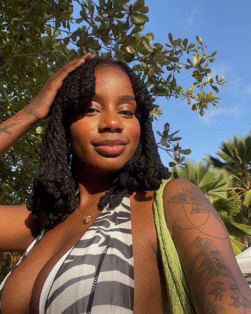 woman with loc knots styled with bangs. looking at camera with hand on head and tree in the background